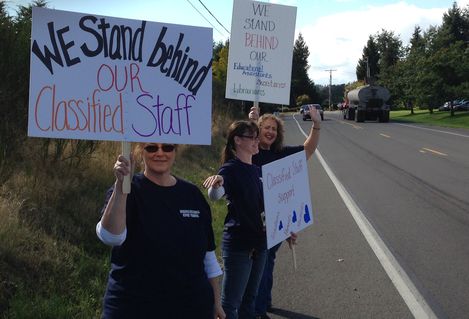 A picketter holds a sign reading "We stand behind our classified staff"